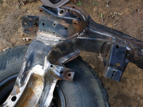 1976 Chevrolet Corvette - A heavily rusted car frame, showing signs of repair with welding, rests on the ground next to a tire.
