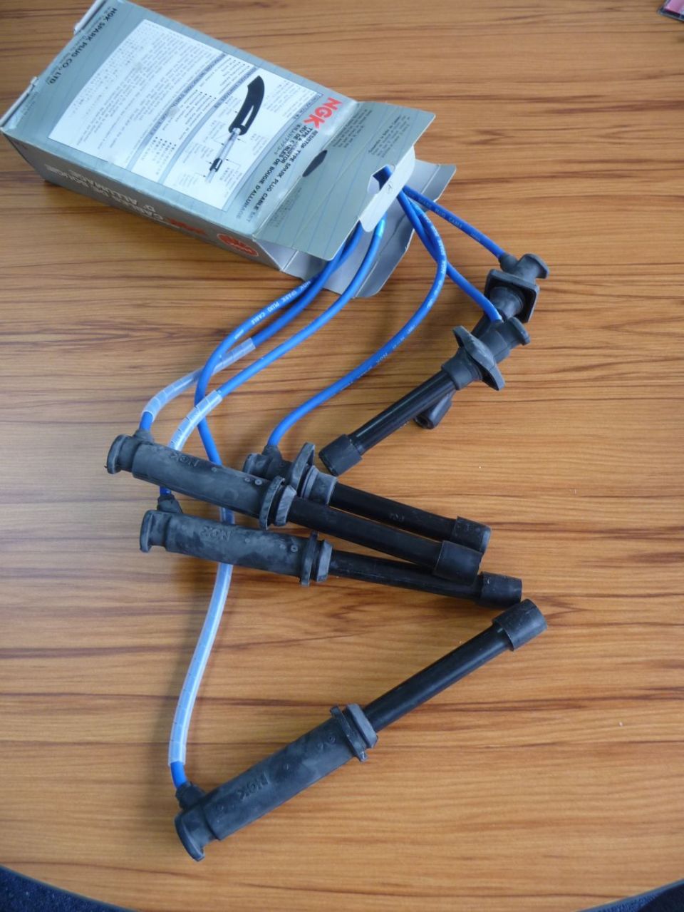 NGK spark plug wires spilling from a cardboard box on a wooden surface