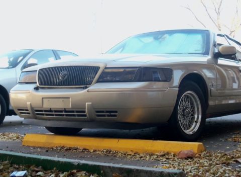 2000 Mercury Grand Marquis - The front grille and headlights of a Mercury Grand Marquis are visible, parked in a lot with fallen leaves.