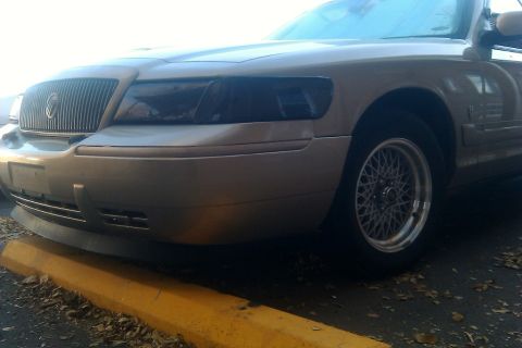 2000 Mercury Grand Marquis - A gold 2000 Mercury Grand Marquis is shown from the front quarter angle, dark tinted headlights and wire-spoke wheels.