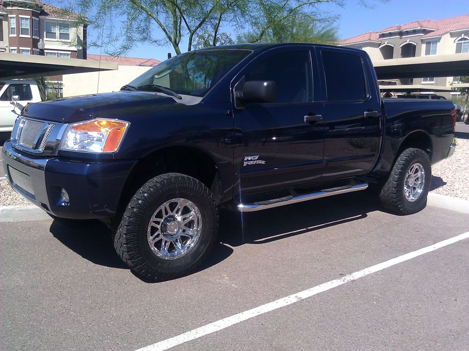 Dark blue pickup truck parked in a lot. It has chrome wheels and side steps