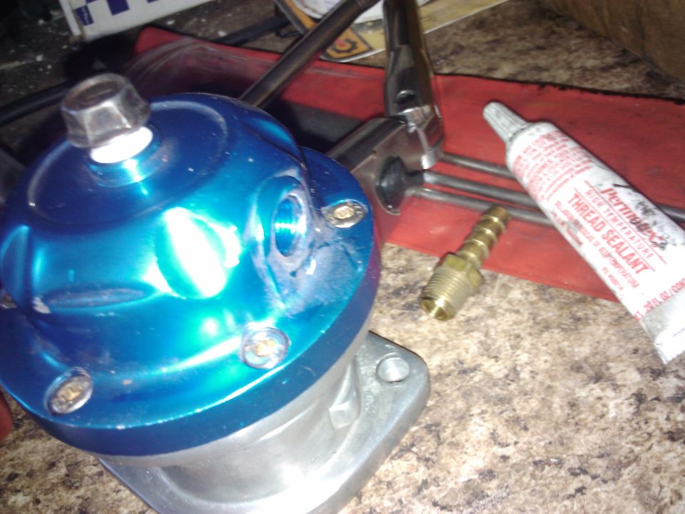Blue automotive part with brass fittings and Permatex thread sealant tube on a speckled surface