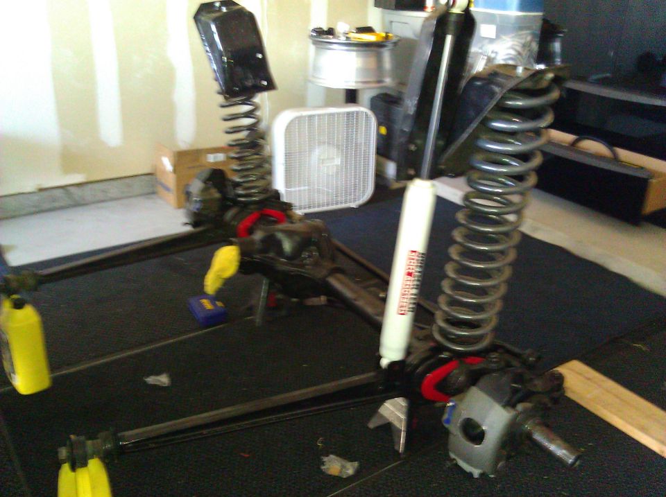 Front axle assembly with shocks and springs, laid out on a garage floor