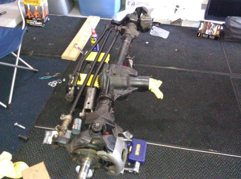 1995 Ford Bronco - A disassembled front axle assembly is laid out on a carpeted floor, with tools and parts scattered around.