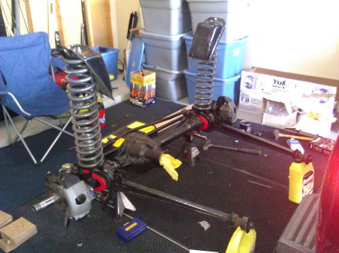 1995 Ford Bronco - Front axle and suspension components are laid out on the floor, likely for repair or modification.
