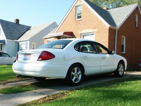 2001 Ford Taurus - A white 2001 Ford Taurus sedan is parked in a driveway in front of a brick house.