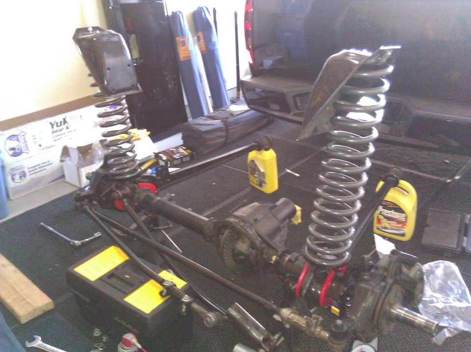 Vehicle suspension parts, including springs and axles, laid out on a garage floor