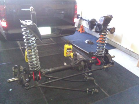 1995 Ford Bronco - Front axle and suspension components are laid out on the floor in front of a black pickup truck.