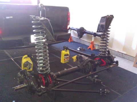 1995 Ford Bronco - Front suspension and axle assembly, likely for a truck or SUV, sits on a garage floor next to bottles of fluid.