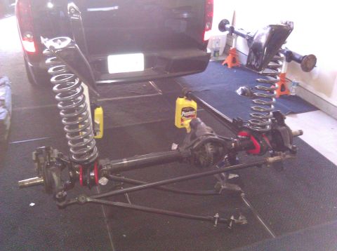 1995 Ford Bronco - Front axle and suspension components are laid out for work, with a black SUV in the background.