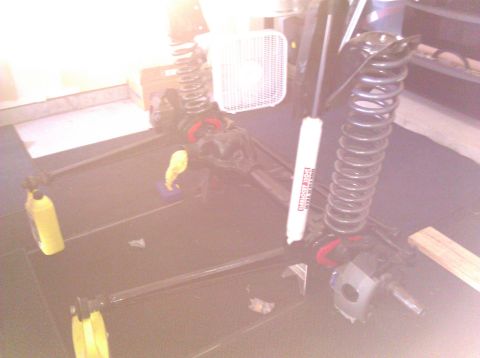 1995 Ford Bronco - Suspension components are laid out on a dark surface, possibly for repair or modification. A fan is visible in the background.