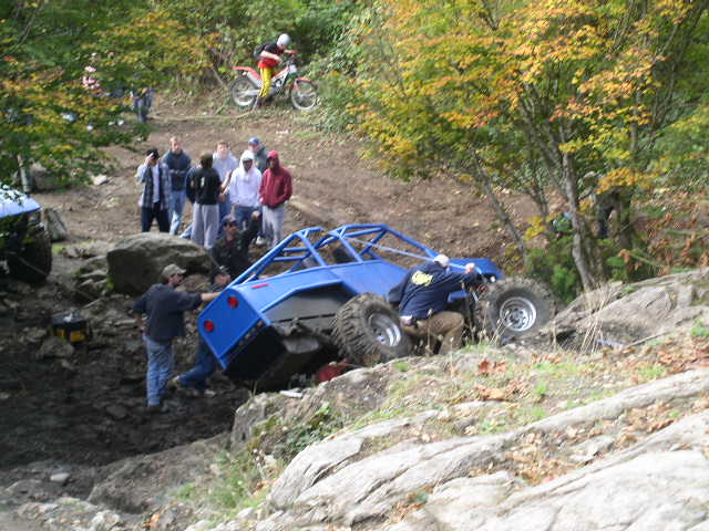 Blue tube-chassis rock buggy climbing boulders on a wooded trail