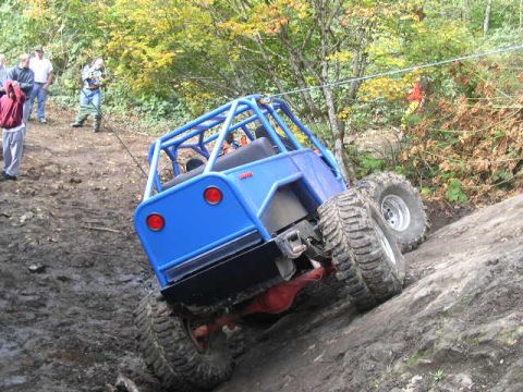 1979 Ford Bronco - A blue off-road vehicle navigates a challenging muddy terrain with large tires.
