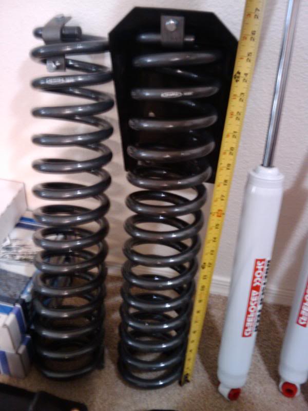 Two black coil springs and two white shock absorbers next to a yellow measuring tape