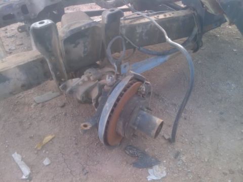 1995 Ford Bronco - A disassembled front axle assembly with brake components lies on the dirt ground.