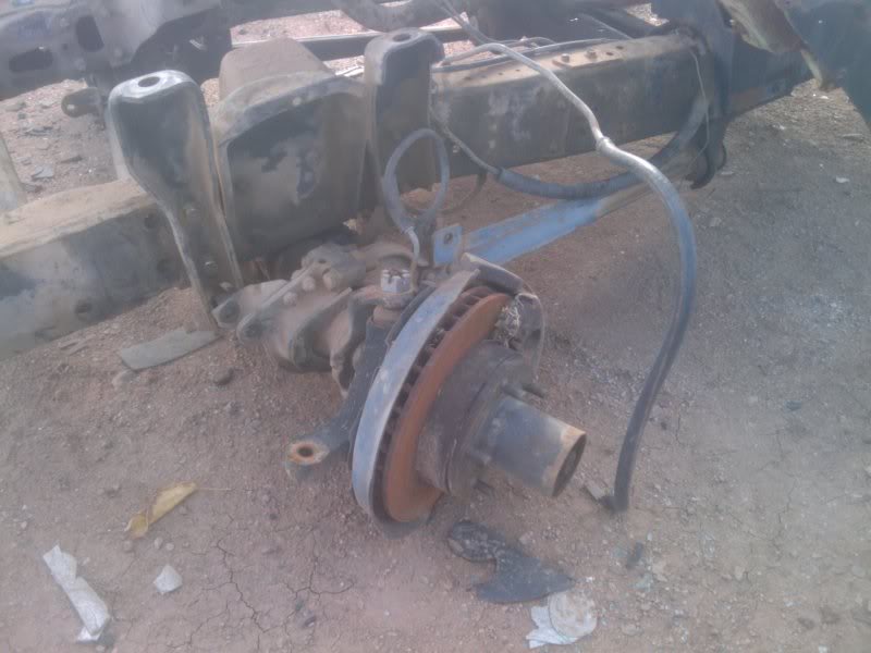 Front axle assembly with rusty brake rotor and suspension parts on the ground