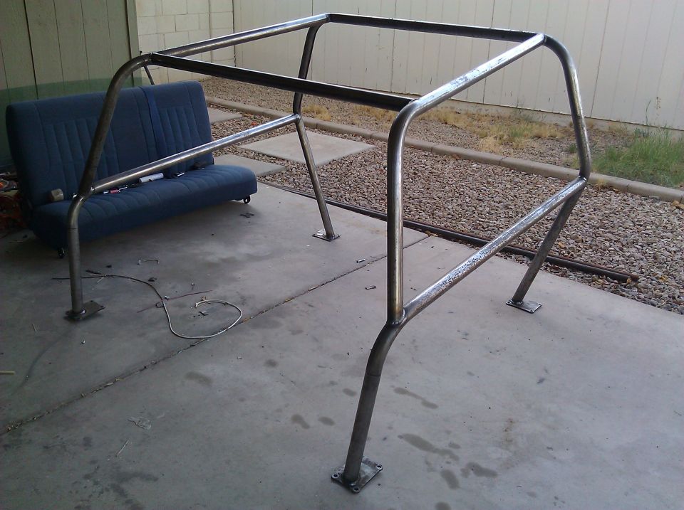 Custom metal roll cage frame on concrete, with a blue vehicle seat in the background