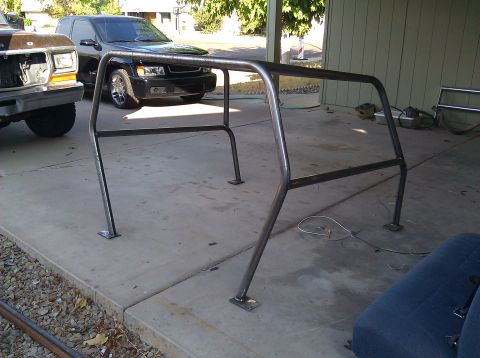1995 Ford Bronco - A custom roll cage is shown in a driveway, with a black SUV and a brown Ford Bronco visible in the background.