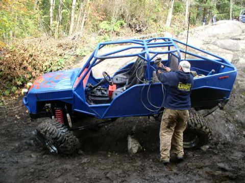 1979 Ford Bronco - A custom-built off-road buggy is being worked on while parked on a wet, muddy trail surrounded by trees.