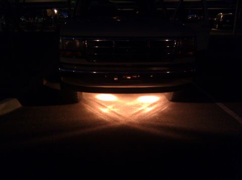 1995 Ford Bronco - The front of a truck is illuminated by its headlights at night.