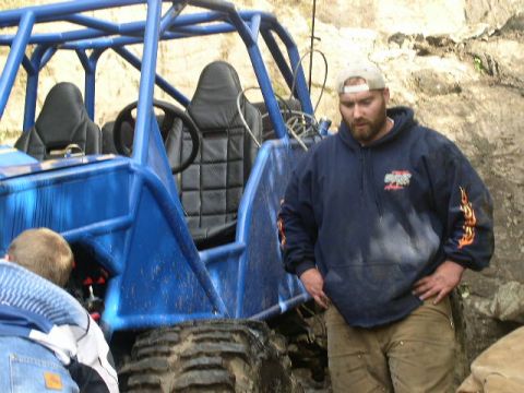 1979 Ford Bronco - A man stands next to a blue off-road buggy with a roll cage and black seats.