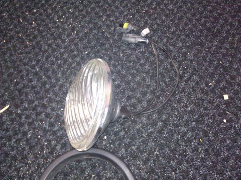 1995 Ford Bronco - Headlight assembly with wiring harness is shown on a dark carpeted surface.