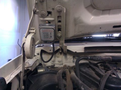 1995 Ford Bronco - An electronic module is attached to the hood structure, with various hoses and engine components visible below.