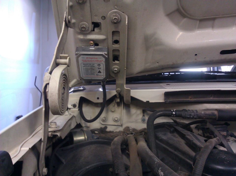 Close-up of an electronic module mounted on the underside of a vehicle's hood near the hinge