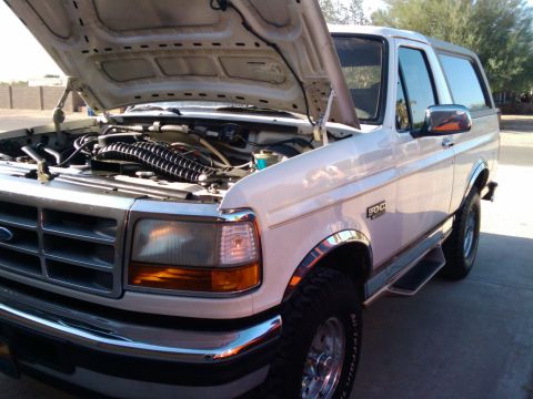 1995 Ford Bronco - White Ford Bronco with hood open, revealing the engine bay. The 'Bronco' badge is visible on the side.