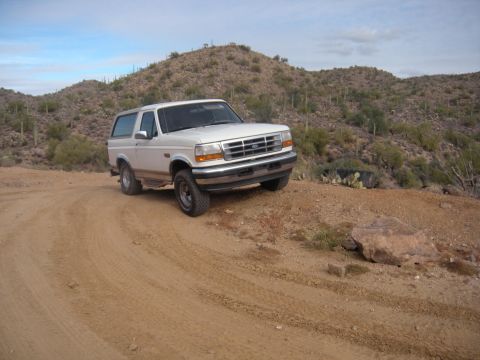 1995 Ford Bronco - White 1995 Ford Bronco parked on a dusty desert road with hills in the background.