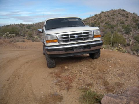 1995 Ford Bronco - A 1995 Ford Bronco sits on a dusty trail with cacti and hills in the background.