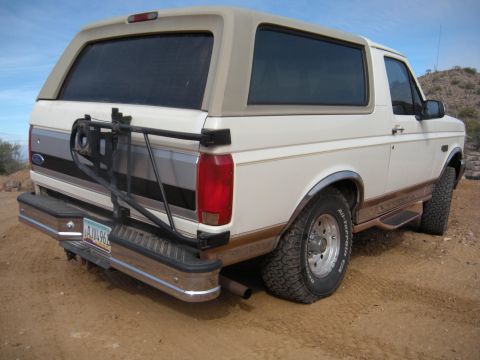 1995 Ford Bronco - Rear view of a 1995 Ford Bronco parked on a dirt road with a spare tire carrier.