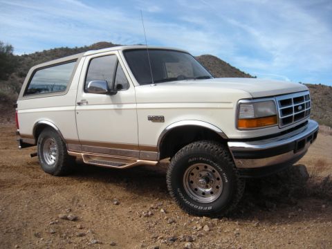 1995 Ford Bronco - This 1995 Ford Bronco is shown in a three-quarter front view, parked on a dirt road with a mountainous backdrop.