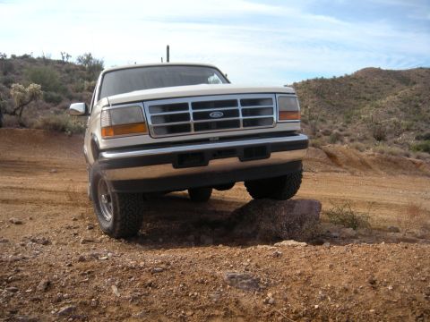 1995 Ford Bronco - A white Ford Bronco navigates a rocky desert landscape, with its front tire resting on a large stone.