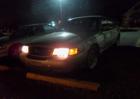 2000 Mercury Grand Marquis - A 2000 Mercury Grand Marquis is parked at night, its headlights illuminating the front grille and bumper.