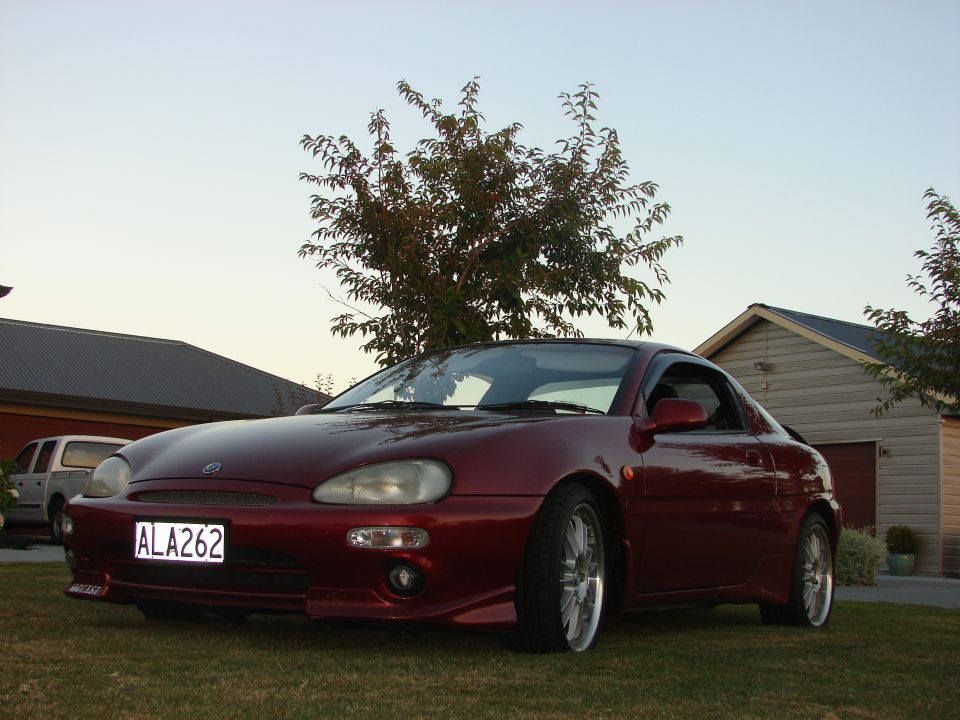 Red coupe parked on grass, front 3/4 view. License plate ALA262