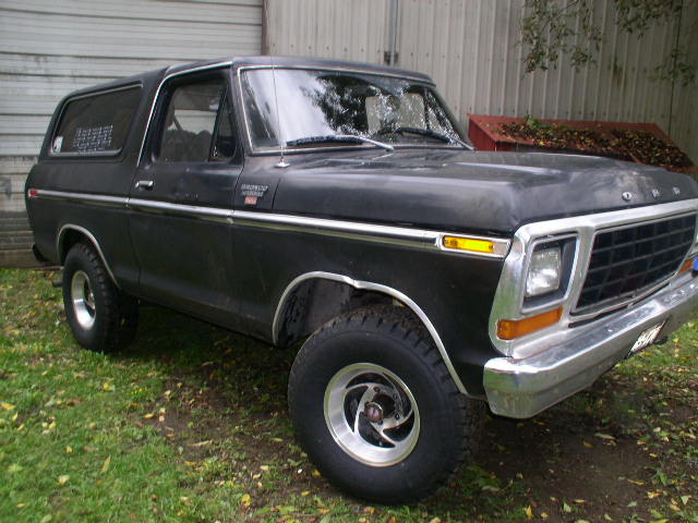 Flat black late-1970s Ford Bronco on grass with chrome grille and polished wheels