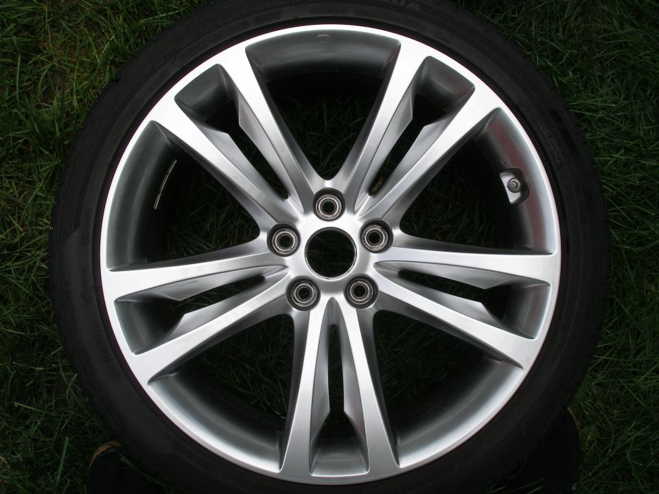Silver alloy wheel with five split spokes and a black tire, resting on grass