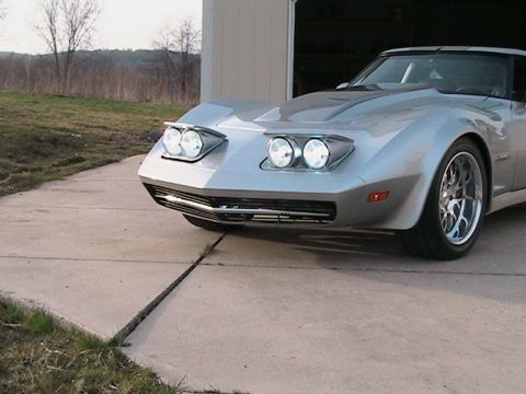 1976 Chevrolet Corvette - Silver sports car with pop-up headlights parked on a concrete driveway.