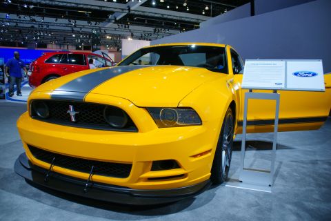 1993 Ford Taurus - Yellow Ford Mustang on display at an auto show, with a red SUV in the background.