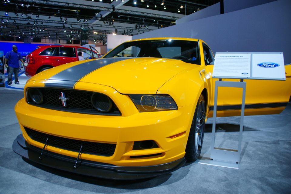Yellow Ford Mustang with grey racing stripes, front view, door open, display sign next to it
