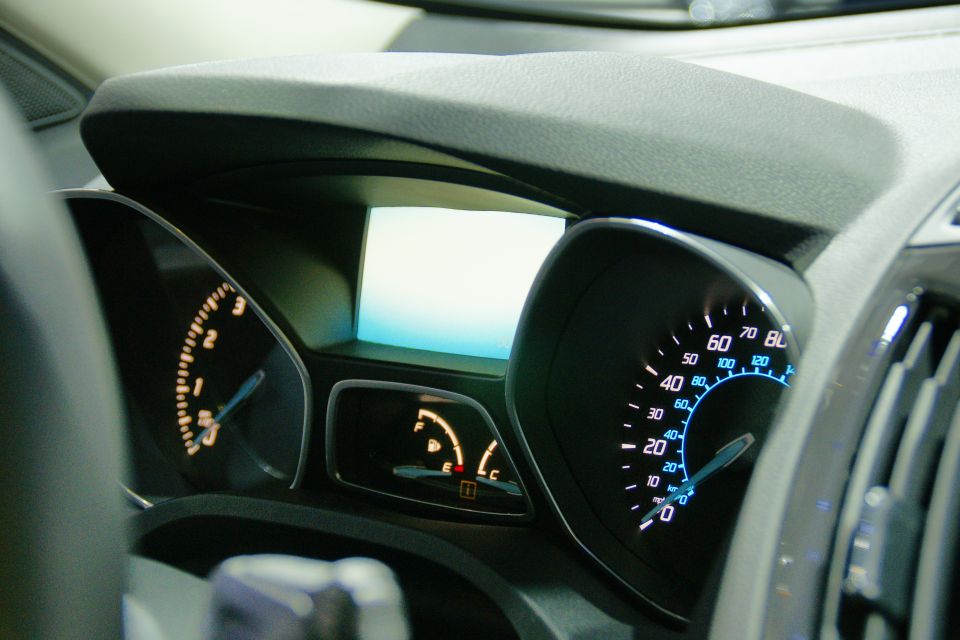Car dashboard showing speedometer, tachometer, and fuel gauge. A small digital screen is in the center