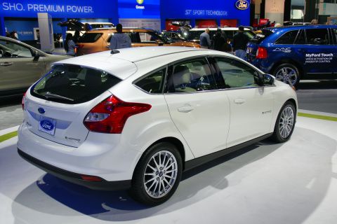 1993 Ford Taurus - White Ford Focus hatchback displayed at an auto show with other vehicles in the background.