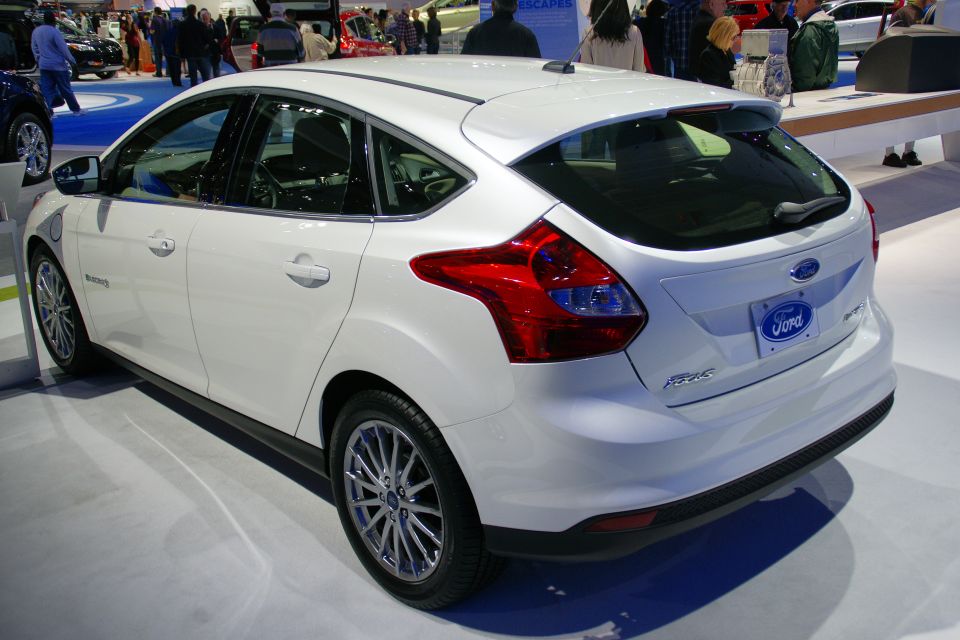 White Ford Focus hatchback with a blue Ford badge on the rear. It has a charging port on the front fender