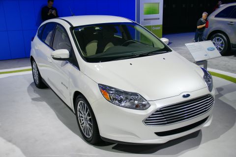 1993 Ford Taurus - A white Ford hatchback is displayed at an auto show with a sign indicating 'Green' technology.