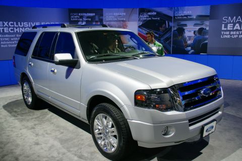 1993 Ford Taurus - A silver Ford Expedition is displayed at an auto show with other Ford models advertised in the background.