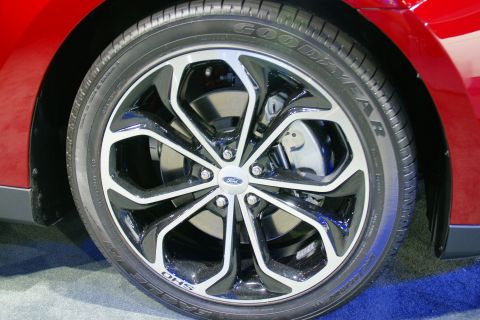 1993 Ford Taurus - Close-up of a red vehicle's wheel, showing a Ford emblem on the alloy rim and Goodyear tire.