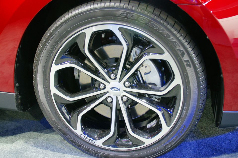 Red car's front wheel with a black and silver alloy rim and Goodyear tire. Ford logo visible on the hub