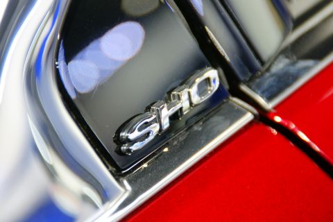 1993 Ford Taurus - Close-up of a SHO badge on a red vehicle, with reflections visible on the chrome and black trim.