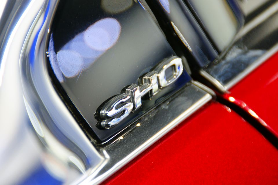 Chrome SHO badge on black trim above red car body panel